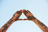 Mit Henna im arabischen Stil bemalte Hände und Arme einer Frau, die mit den Fingern ein Dreieck vor blauem Himmel bilden, Muscat, Oman