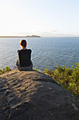 Rückenansicht einer Frau, die auf einem Felsen sitzt, Ilha do Mel, Parana, Brasilien