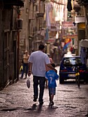 Vater und Sohn gehen auf der Straße der historischen Altstadt spazieren, Rückansicht; Neapel, Italien