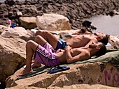 Three Young Man Lying On Shore Rocks; Naples, Italy