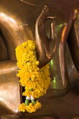 Wat Somdej Phuttachan, Thailand; Nahaufnahme einer geblümten Lei über der Hand einer buddhistischen Statue