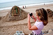 Malecon, Puerto Vallarta, Mexico; Young Girl Taking Photo Of Sand Sculpture