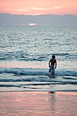 Puerto Vallarta, Mexiko; Junger Mann watet bei Sonnenuntergang im Meer