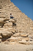 Mann sitzend auf einem Teil einer Pyramide in der Wüste