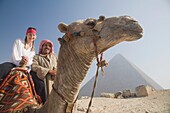 Junge Touristin auf einem Kamel mit einem örtlichen Führer bei den Pyramiden von Gizeh, Kairo, Ägypten