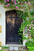 Roses Growing Around The Old, Wooden Door Of A Stone House