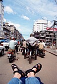 Tourist's Feet On A Rickshaw In A Busy Street Scene