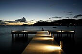 Frau sitzt am Ende eines Piers in der Abenddämmerung