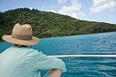 Frau mit Hut sitzt auf dem Deck eines Segelboots und schaut auf eine Insel