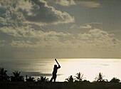 Mann spielt Kricket an der Küste (Silhouette)