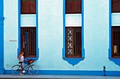 Eine Frau mit ihrem Fahrrad vor einem blauen Gebäude in Bayamo.