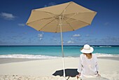 Frau an einem tropischen Strand unter einem Regenschirm sitzend