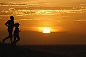 Vater und Sohn beim Laufen auf Sanddünen bei Sonnenuntergang