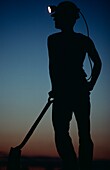 Silhouetted Miner With Lit Hat And Shovel