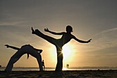 Two Women Silhouetted Doing Capoeira On Beach At Sunset