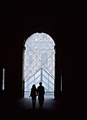 Couple Walking Through Passageway To The Pyramid Of The Louvre Museum