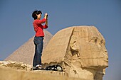 Woman Taking Photograph In Front Of Sphinx And Pyramid