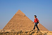 Woman With Rucksack Walking Along Ancient Wall In Front Of Pyramids