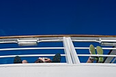 Passengers On Board Cruise Ship Reading With Their Feet Up On The Railings