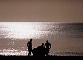 Drei Männer in Silhouette und Boot am Strand