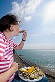 Frau isst Austern neben dem Meer in Cancale