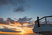 A Female Passenger On The Top Deck Of Cruise Ship Watching Sunset