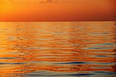 Ruhige Meeresoberfläche mit orangefarbenem Sonnenuntergang, flacher Blickwinkel