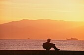Backpacker In Silhouette Sitting By Coast
