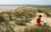Junges Mädchen spielt auf einer Sanddüne mit Eimer und Spaten