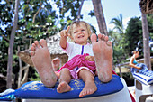 Daughter Sitting Between Father's Feet On Sun Lounger