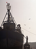 Man Painting Fishing Boat On The Harbourside At Dusk