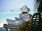 Frau mit Hut im Schatten am Strand sitzend