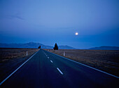 Leere Straße durch die Landschaft bei Nacht mit Mond