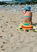 Junge Frau im Bikini auf einem Handtuch am Strand sitzend