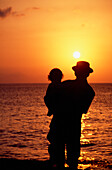 Silhouette von Vater und Kind, die im Meer stehen und den Sonnenuntergang beobachten