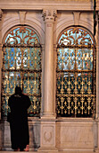 Frau im Tschador-Schleier schaut in das Fenster der Omayyaden-Moschee