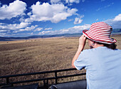 Frau beobachtet Tiere im Ngorogoro-Nationalpark durch ein Fernglas