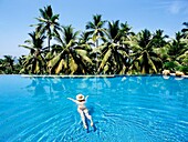 Frau schwimmt im Pool unter Palmen