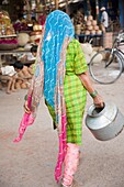 Frau in buntem Sari trägt einen Metallkrug