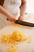 Koch bei der Herstellung von Tagliatelli, indem er ein aufgerolltes Nudelblatt schneidet, La Vecchia Scuola