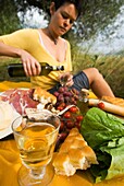 Frau gießt eine Flasche Wein in Vorbereitung auf ein Picknick unter Olivenbäumen ein