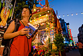 Backpacker With Guidebook In Front Of Roadside Shrine At Dusk