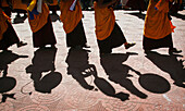 Mönche in traditioneller Kleidung mit gelb-orangefarbenen Hüten und Gewändern tanzen und schlagen Trommeln, Blickwinkel unten