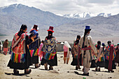 Menschen in traditioneller Kleidung und Hüten gehen unterhalb der Berge