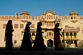 Silhouette von vier Frauen in Saris, die an einem alten Gebäude vorbeigehen