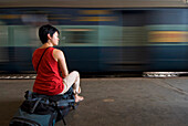 Backpacker Sitting On Rucksack In Train Station, Blurred Motion
