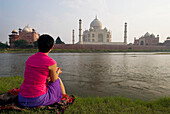 Tourist sitzt am Ufer des Yamuna-Flusses und bewundert das Taj Mahal