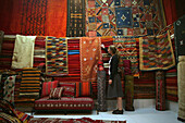 Junge Frau stöbert in einem Marktstand im Souk nach marokkanischen Teppichen und Vorhängen.