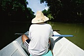 Mann mit Strohhut in einem Boot, das einen Fluss hinunterfährt