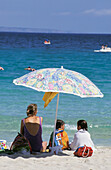 Mother With Daughters Under Umbrella On The Beach